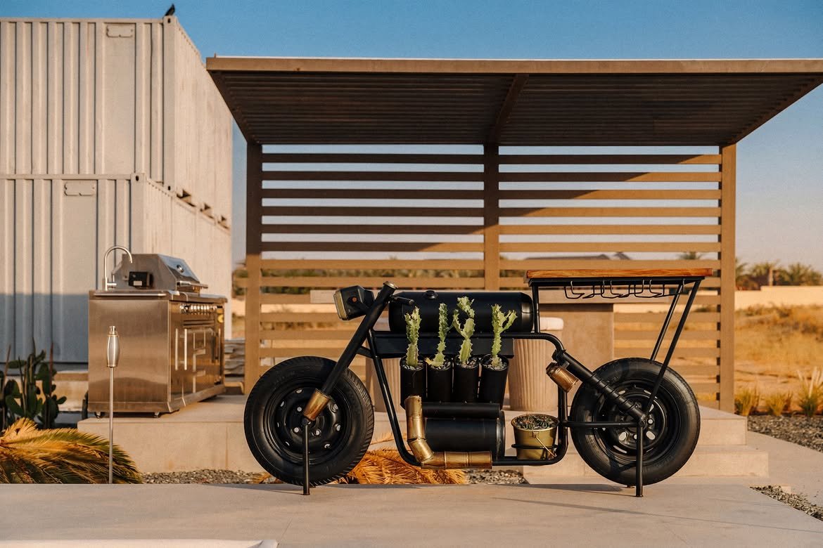 A custom motorcycle under a slatted pergola beside the outdoor kitchen