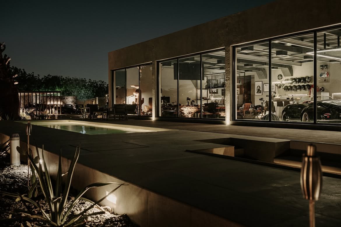 The same glass facade, lit from within and mirrored in the pool after dark