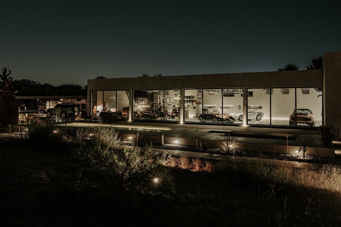 The long showroom glowing through its glass wall at night, cars inside